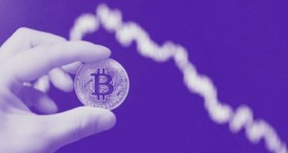 Bitcoin Münze in einer Hand gehalten und im Hintergrund fallender Chartverlauf